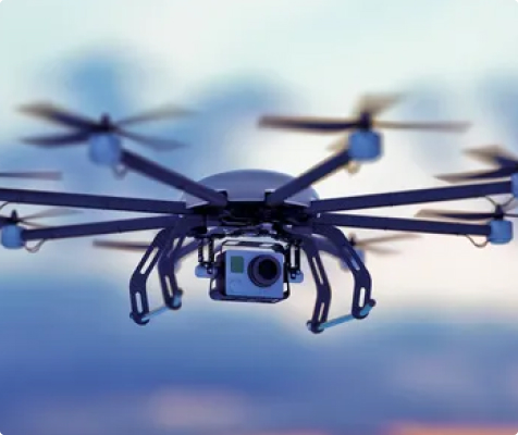 A multi-rotor industrial hexacopter drone equipped with a high-definition gimbal camera system, flying against a blurred sky background for power line and infrastructure inspection.