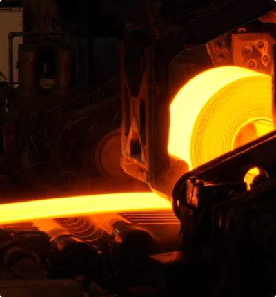 Molten steel glowing orange as it is processed through industrial rolling machinery inside a steel manufacturing plant.