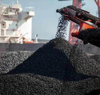 Coal being unloaded from heavy industrial equipment onto a large pile at a port or coal handling facility.