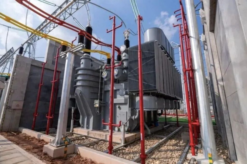 High-voltage power transformer installed in an electrical substation with cooling radiators, insulated bushings, and overhead transmission connections.