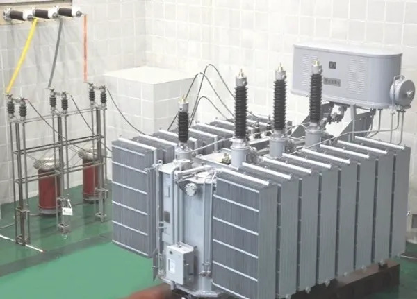 High-voltage power transformer installed at an electrical substation with bushings, cooling radiators, and overhead transmission connections.