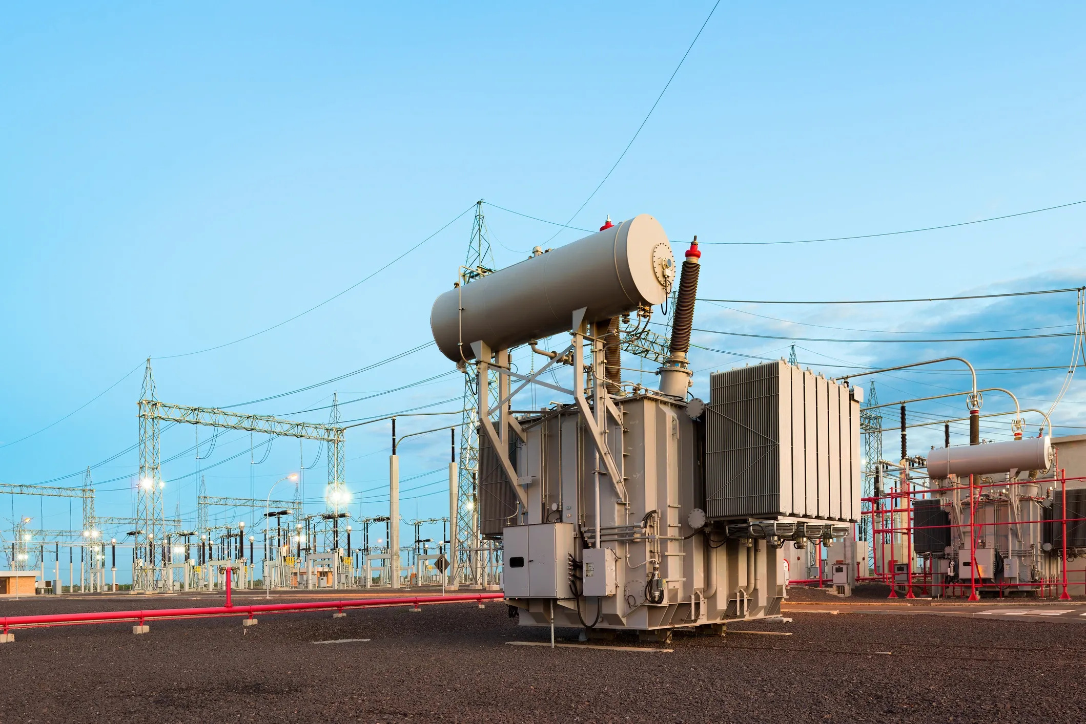 High-voltage power transformer installed at an electrical substation with bushings, cooling radiators, and overhead transmission connections.